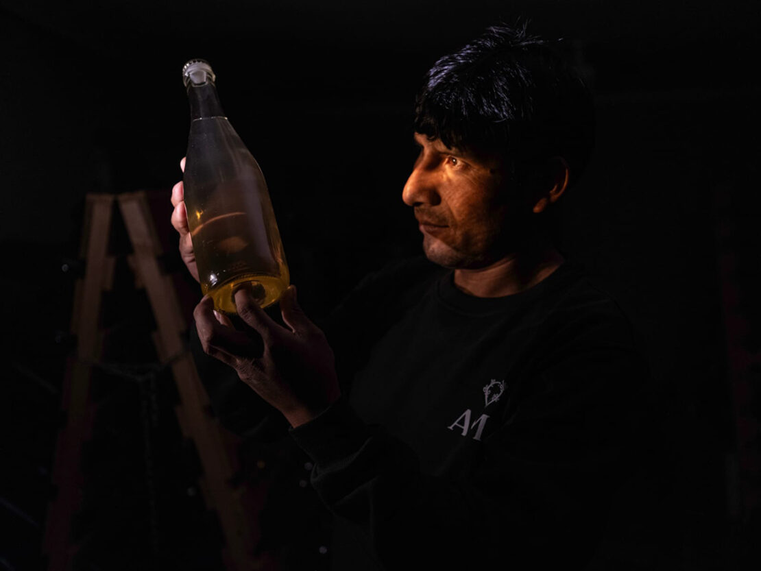 Manuel Choqque Bravo observando a contraluz una botella de fermentado Oxalis en su bodega.
