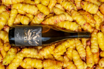 Botella de Oxalis, bebida fermentada de oca andina, sobre un lecho de tubérculos amarillos cosechados en Cusco, Perú.